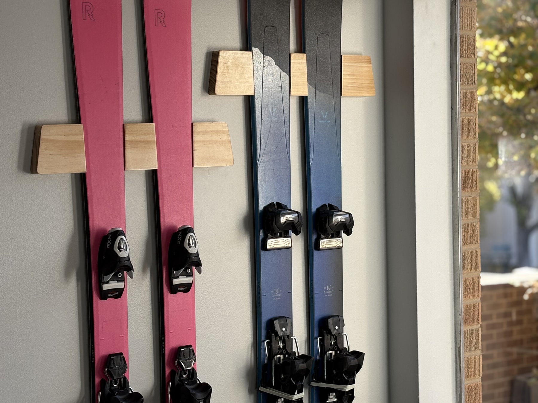 Pink and blue skis mounted on Adventure Mounts Vert Chaser wood ski mount showcasing the premium clear coat finish quality.
