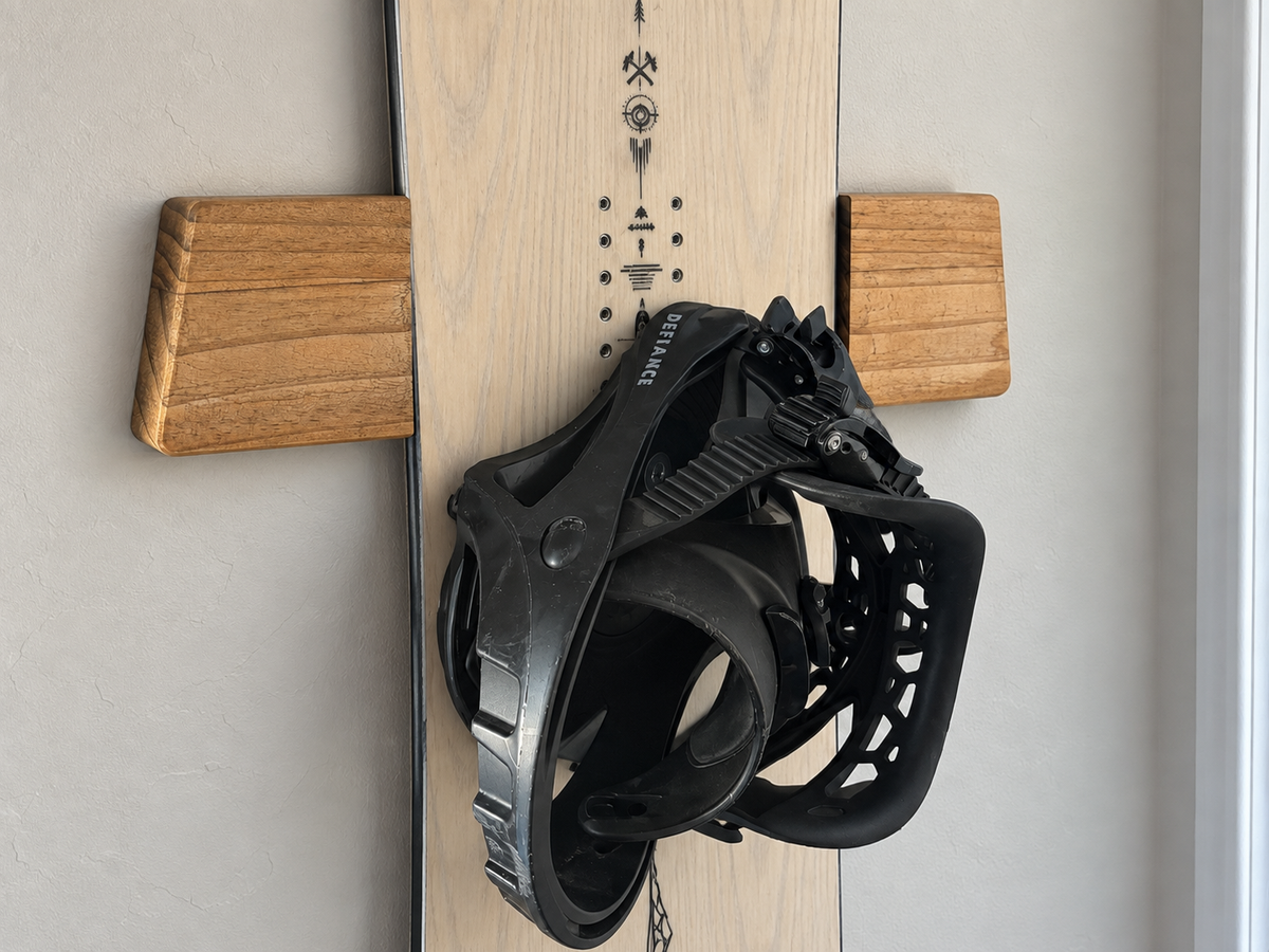 Close-up of a wood wall mount behind a vertically displayed snowboard with a black binding